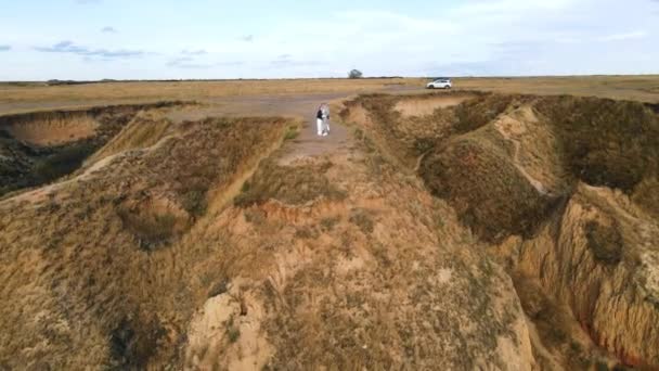 Boven het zicht van een jong koppel dat dichtbij staat, omhelzend op een hoge heuvel van de kust. Luchtfoto van man en vrouw strelend teder elkaar op klif boven zee in het zonlicht. Begrip landschap — Stockvideo