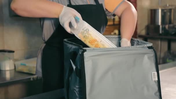 Ambalarea alimentelor într-o pungă termică. Lucrătorii din bucătărie scufundă mâncarea caldă în recipiente într-o pungă termică pentru livrare ulterioară. Livrarea alimentelor — Videoclip de stoc