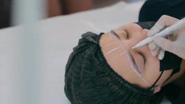 Kalıcı makyaj ustası bir kadın müşteriye kaş yapar. Kaş dövmesi yakın çekim. Kalıcı makyajla kaşları işaretlemek ve yaratmak