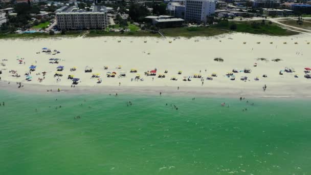 Полеты над пляжем и купание людей в море в жаркое лето. Люди сидят под жёлтыми зонтиками, прячась от солнца. Начало туристического сезона и пляжного сезона. — стоковое видео