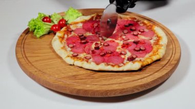 Pizza dilimini tahta kesme tahtasının üzerinde pizza kesici tekerleğiyle üçgenlere ayırmak. İnsan elinin siyah eldivenli beyaz masada pizza dilimini ayırdığı görüntüyü kapat. Yiyecek kavramı