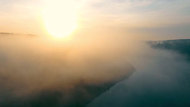 Fantastique paysage de rivière brumeuse dans des poutres ensoleillées. Vue aérienne depuis un drone de mystérieuse vallée avec une rivière brouillard sinueuse qui coule entre des collines avec un coucher de soleil pittoresque sur le fond. Concept de paysage — Video