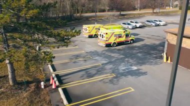 Ambulans araçları hastanenin acil servis otoparkında. Üç sarı ambulansla gündüz vakti hastane otoparkından ayrılmaya hazırlanan hava görüntüsü. Hayat kurtarma kavramı