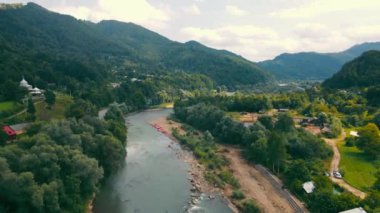 Yoğun orman ve dağların arasından akan başıboş bir nehir. Ukrayna, Karpatlar 'daki tepeler ve küçük köyler arasında akan dağ nehrinin insansız hava aracı görüntüsü. Manzara kavramı