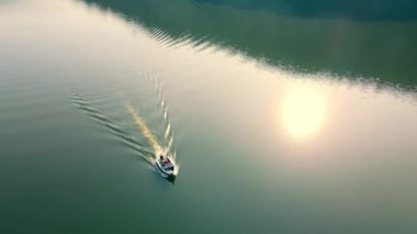 Karanlık nehirde seyreden küçük sürat teknesi, alacakaranlıkta suyun üstünde iz bırakıyor. Sonbaharda günbatımında sakin gölde kayalık kıyılarda seyreden su tekneleri. Su aktiviteleri kavramı.