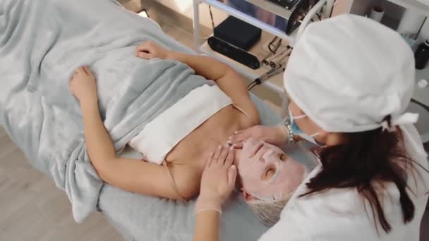 Massage und Heilmaske beim Kosmetikerin-Arzt. Die Kosmetikerin führt eine Massage durch, um die Patientin bloßzustellen. Eine gesunde beruhigende Maske auf dem Gesicht eines Patienten. — Stockvideo