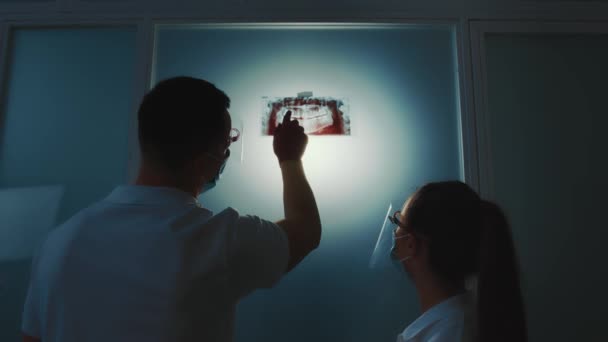 Dois dentistas olham para uma radiografia panorâmica da lacuna dentária em uma sala escura. — Vídeo de Stock