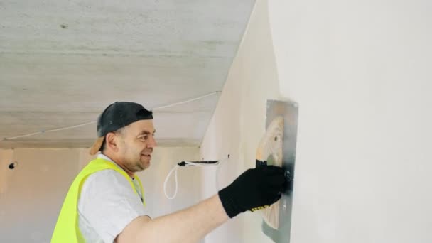 El maestro de la reparación de los apartamentos alinea las paredes con el estuco. Trabajos de pintura y enlucido en obras de construcción. — Vídeo de stock