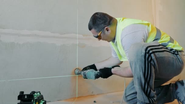 Construction worker drills a hole in the wall under the socket. The level of the hole for the electrical outlet is set by a laser. — Stock Video