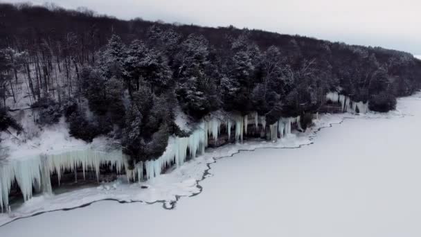 Voo aéreo sobre o penhasco perto do lago do qual pendurar enormes icicles. Lago congelado e cascata congelada. — Vídeo de Stock