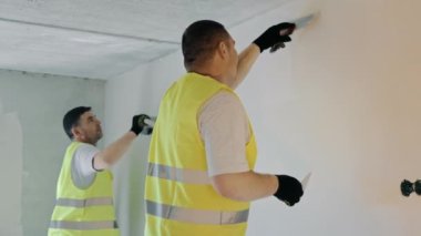 İki usta apartman dairesinde tamirat işi yapıyor. Uzman ressamlar odanın duvarını alçılıyor.