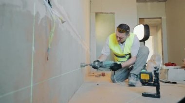 En üstteki inşaat işçisinin görüntüsü prizin altındaki duvarı deliyor. Elektrik prizi için delik düzeyi lazerle ayarlanıyor.