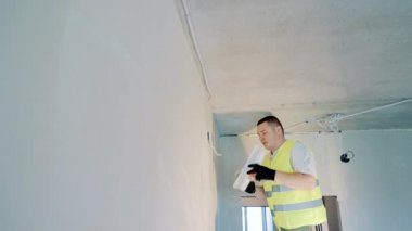 A labor migrant of Caucasian appearance carries out plastering and painting work in a room. Renovation of the room