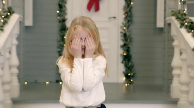 Gözlerini kapayan ve kameraya şaşkınlıkla bakan bir kız çocuğu. Yeni yıl süsleri olan bir evin yakınındaki beyaz bir çocuğun duyguları.