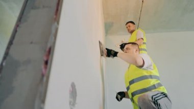 İki usta apartman dairesinde tamirat işi yapıyor. Uzman ressamlar odanın duvarını alçılıyor.