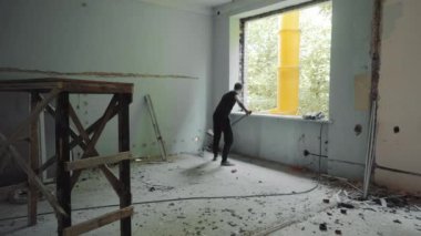 Cleaning the room from construction debris. The construction worker, the cleaner, throws building stones through the window into a special sleeve with a shovel.
