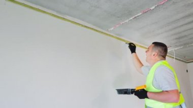 The man is a painter, painting the top of the wall with white paint and a brush