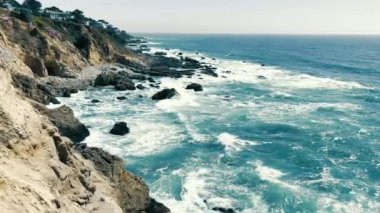 Rocky coast of the Pacific Ocean. Sea waves crash against the rocky coast. A sunny day and a beautiful view of the ocean