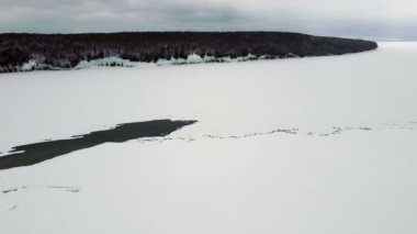 Flying over a frozen lake on a cloudy day. The Great Lake is covered with ice and snow. The middle of the lake is ice-free. Spring floods on the lake. Climate change in winter.