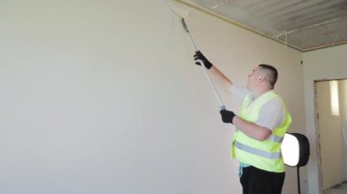 A man paints a wall in a room white. Repair work in the room of the house. The painter rolls white paint on the wall with a roller