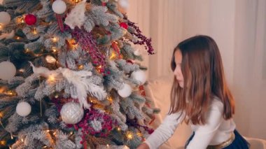 A little girl decorates a Christmas tree. Close-up of childrens hands clinging to a silver ball on a Christmas tree. New Year decorations.