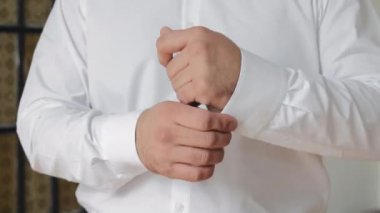 Beyaz gömlekli bir adam kolundaki düğmeleri bağlar. Otelde bir iş adamı sabahı.