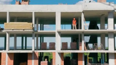 Tek katlı, çok katlı bir binanın havadan görünüşü. İnşaat işçileri farklı katlardaki inşaat alanında çalışıyorlar. Yerde çalış, yan gözle bak.