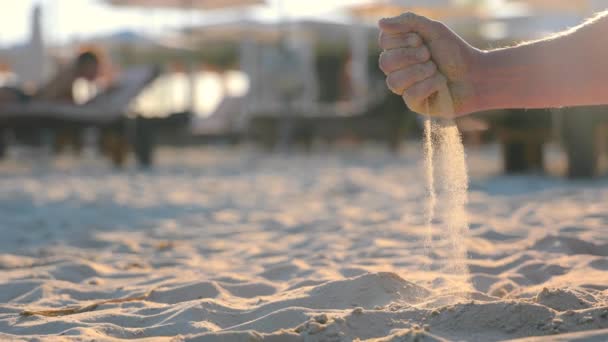 男のクローズアップは 彼の手に砂を保持し ゆっくりとそれを注ぐ 対照的な太陽は 砂の落下粒子を照らし出します 経過時間の模倣 — ストック動画