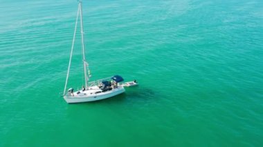Mavi sudaki lüks beyaz yatın havadan görünüşü. Tekneli renkli manzara, körfez, berrak gök mavisi suyu. Havadan üst görüntü. Motorlu deniz manzaralı.
