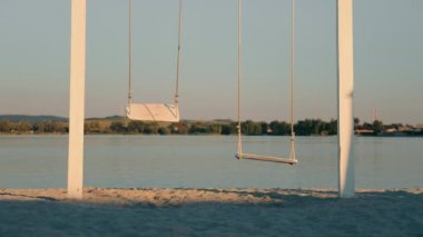 Yalnızlık ve yalnızlık kavramı. Yalnız bir oyuncak ayı salıncakta sallanıyor. İki salıncak, birinde bir oyuncak ayı gölün arka planında oturuyor.