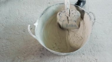 Kovadaki kürekle betonu karıştırmak. İnşaatçı bir kürekle çimento havanını yavaşça karıştırır..