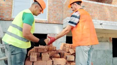 İnşaat işçileri bütün tuğla parçalarını seçiyorlar. Bir tuğla ev inşaatı