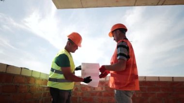 İnşaat alanındaki mimarlar bina planını ve çizimlerini yakından inceliyor. Mimari planla diyalog ve eylem planı