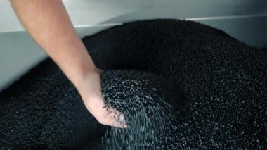 Bir adam yakın plan plastik granülleri eliyle topluyor. Lastik ürünlerin üretimi için ham madde