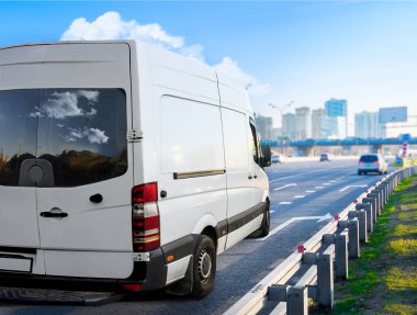 Beyaz minibüs şehir planında otoyolda ilerliyor..