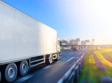 Beyaz römorklu büyük bir kamyon şehre doğru gidiyor.