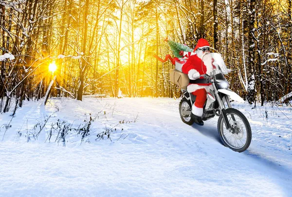 Papai Noel montando uma moto entregando presentes de Natal ou Ano Novo, parcelas na paisagem de inverno de neve ao pôr do sol — Fotografia de Stock