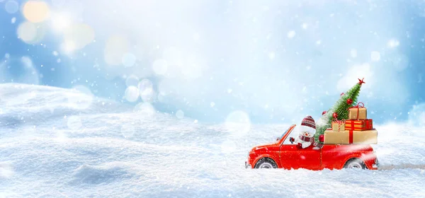 Schneemann im roten Auto liefert Weihnachtsbaum und Geschenke im Winter Schnee Hintergrund. — Stockfoto