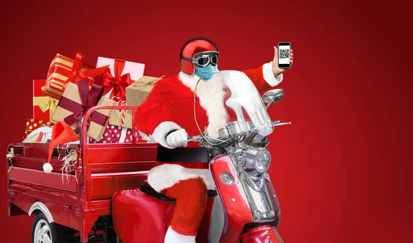 Święty Mikołaj w masce medycznej pokazać kod QR na smartfonie zaszczepiony COVID-19 dostarczanie prezentów świątecznych lub noworocznych na czerwonym skuterze na czerwonym tle — Zdjęcie stockowe