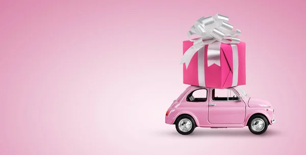 Pink toy car with gift box on a roof on pink background. Copy space. — Fotografia de Stock