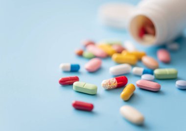 Beyaz plastik ilaç kutusundan saçılmış çok renkli haplar.