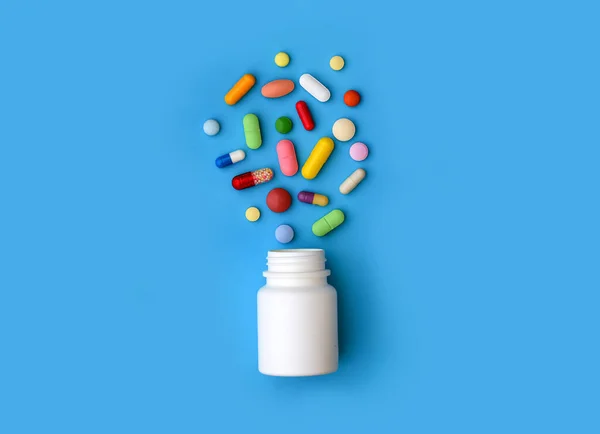 Assorted Pills and white plastic pills bottle on blue — Stock Photo, Image