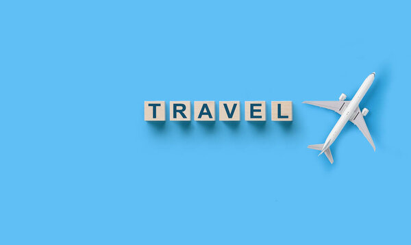 Wooden cubes with TRAVEL word and toy airplane model on blank blue background. Flat lay. Traveling concept