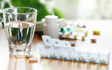Masada bir bardak su bulunan günlük vitamin ve ilaç düzenleyicisi..