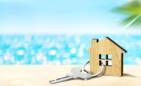 Model of house and key on sandy beach with sea and sky on the background
