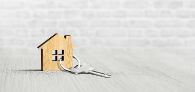 Tuğla duvar arka planının yanındaki beyaz masada anahtarı olan anahtarlık evi. Emlak, sigorta konsepti, ipotek.