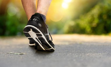 Legs of a jogger in shoes close-up in the park at sunset