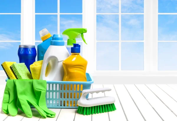 Household cleaning supplies in plastic basket on the white table over the window and sky background