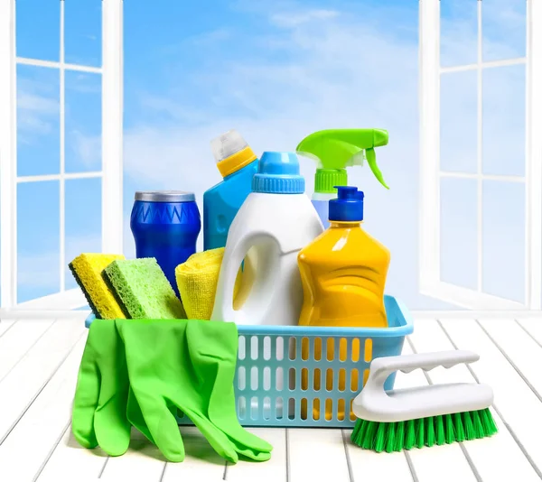 Household cleaning supplies in plastic basket on the white table over the open window and sky background. Copy space