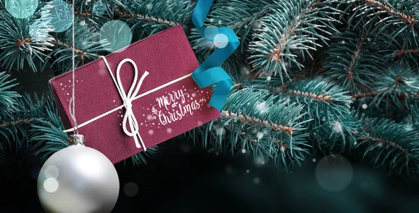 Merry Christmas greeting card or web banner with lettering. Gift box on blue christmas tree background.